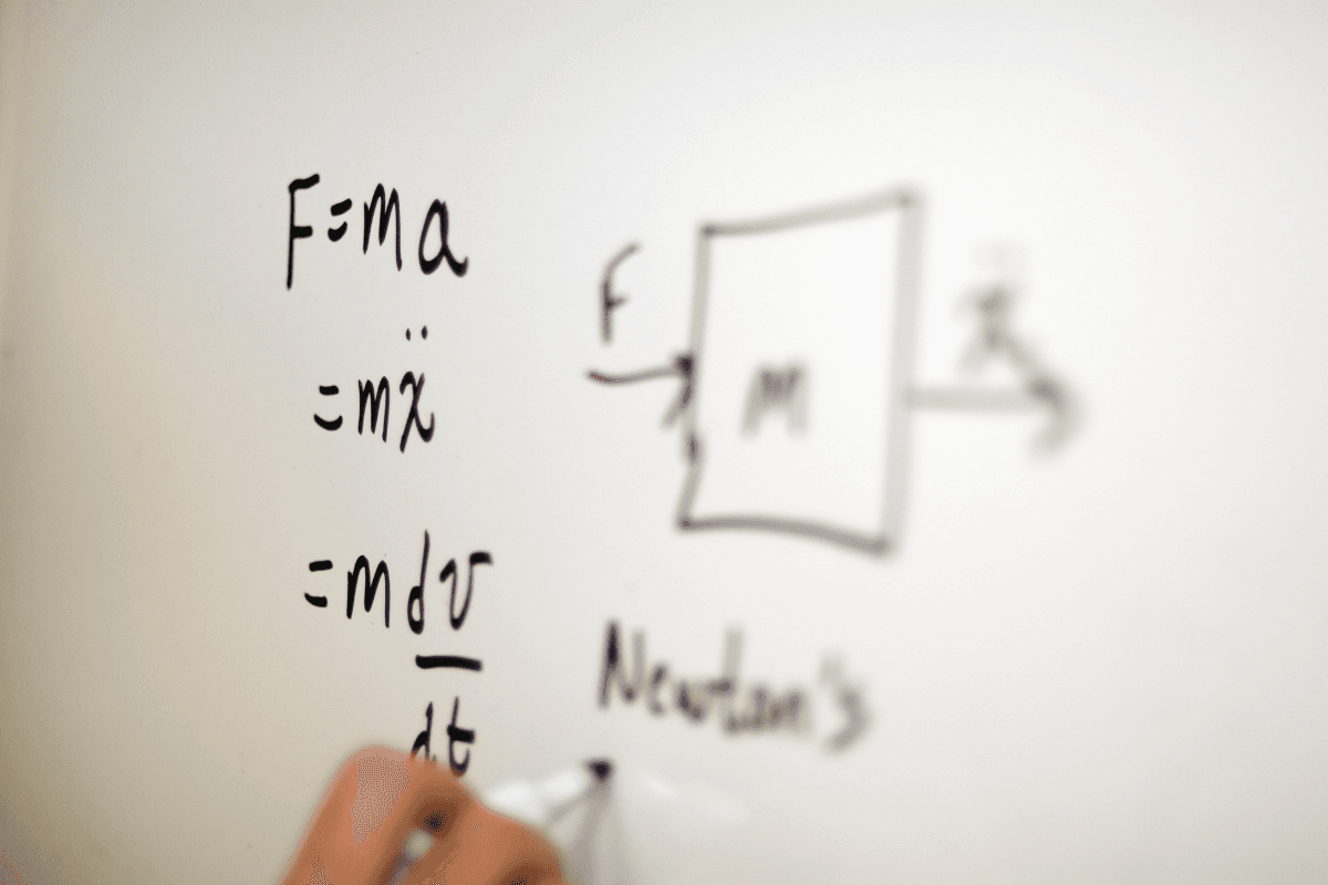 A hand writing Newton's second law on a whiteboard